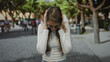© Krakenimages.com - Woman covering ears and holding head, wearing glasses and a white top on a city street lined with trees and pedestrians, reacting to noise and commotion; urban frustration.