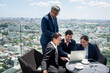 © chachamp - Business team working together on a laptop at outdoor or rooftop office with city background