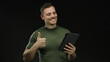 © Krakenimages.com - Young man in green shirt holds tablet and gestures thumbs up against dark background, conveying positive and interactive atmosphere, focusing on technology and expressions.