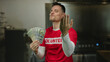 © Krakenimages.com - Young man in hotel holding american dollars with confident gesture wearing red shirt indoors showcasing wealth and inviting engagement in a casual setting.