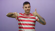 © Krakenimages.com - Young man with tattoos in striped shirt against purple background showing mixed thumbs up and down gesture with a smile suggesting decision making and evaluation
