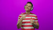 © Krakenimages.com - Man smiling with headphones gives thumbs up in a striped shirt against a vibrant pink background, expressing positive emotion and enjoyment.