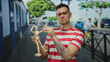 © Krakenimages.com - Man with tattoo holding wooden model in urban street background wearing glasses and striped shirt.