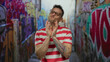 © Krakenimages.com - Man smiling outside with graffiti in urban setting, wearing striped shirt and glasses in city street.