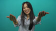 © Krakenimages.com - Young chinese woman pointing and gesturing 'come here' against an isolated green background wall, expressing a friendly and inviting demeanor in a casual setting.