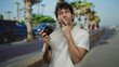 © Krakenimages.com - Man outdoors on street pondering with camera in hand, palm trees lining the background suggesting a warm, tropical location ideal for photography.