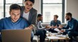 © patricia - A man on a laptop is assisted by a woman pointing at the screen in a contemporary office setting with blurred colleagues in the background