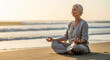 © SYATRI RAWU - Peaceful senior woman practicing mindfulness and deep meditation in a yoga lotus posture on a serene beach during a beautiful sunrise