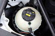 © Best Auto Photo - Close-up of modern car coolant reservoir with black cap marked by warning labels and yellow arrows, showing essential engine maintenance component under hood. Car cooling system.
