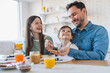 © InsideCreativeHouse - Family of three with little son sharing a joyful morning meal around the kitchen table enjoying tasty food and drinking orange juice. Caucasian family enjoy breakfast together in modern apartment.