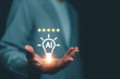 © panya7 - Businessman holding glowing AI light bulb icon with five stars above, symbolizing artificial intelligence excellence, innovation, smart solutions and digital technology concepts.