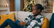 © ABCreative - A young woman is sitting on a couch, focused on a book with a blue cover. She reads intently, reflecting deeply, and bites her lip in concentration. A Christmas tree flickers softly behind her.