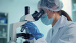 © Avelino - Young female researcher observing samples through microscope with surgical cap, mask and gloves. Generated with AI