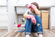 © Maria - Woman sitting near leaking sink in laundry room holding adjustable wrench