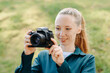© Anton Pentegov - black dslr camera in hands, young pretty redhead caucasian woman photographer in green shirt at work outdoors in sunny summer day, smiling widely