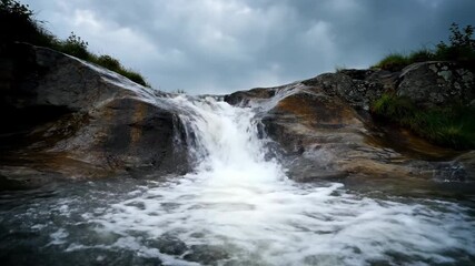 Wall Mural - A tracking shot follows a stream of rainwater flowing rapidly down a natural rock formation, highlighting the power of nature under stormy skies rapidly, Tracking shot, wild
