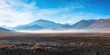 © Pcs - A vast, barren landscape with mountains in the distance, a thin layer of fog or mist in the foreground, and a clear blue sky above.