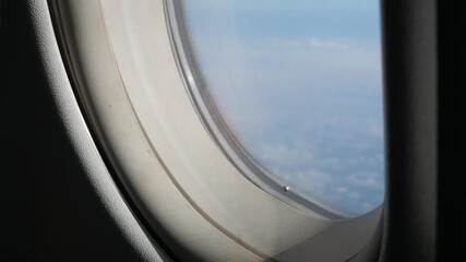 Wall Mural - view through airplane window above the clouds and sky inspiration concept in cinematic aerial flying over white fluffy cloudscape in high altitude sky with fresh clean air and blue skies