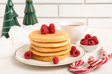 Wall Mural - Plate of sweet pancakes with raspberries, candy canes, cup of tea and Christmas trees on white table