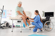 © Pixel-Shot - Senior man with therapist putting on knee pad in rehabilitation center