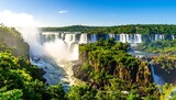 Panoramic view of Iguazu Falls. Lush green jungle surrounds cascading waterfalls under a vibrant blue sky