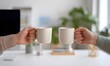 © simba kim - Symmetrical framing focusing on the space between two coworkers. They are clinking their coffee cups together in a casual cheers moment.