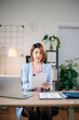 © laddawan - Confident Asian businesswoman multitasking with tablet and laptop in bright office. Ideal for business, technology, consulting, digital work, leadership