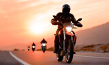 Motorcyclist in black gear rides along winding road at sunset, with silhouettes of fellow riders in the background, capturing the thrill of adventure and freedom on two wheels