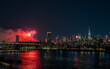 © Travel 'n' Lifestyle - July 4th. View of vibrant fireworks exploding over the dark waters reflecting city lights, illuminating the skyline and bridge in New York, New York, United States.