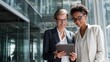 © Md - Two professional women collaborating on a tablet device in a modern office environment discussing business strategy