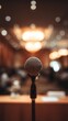 © KN Studio - Microphone on Stage: A close-up captures a sleek microphone poised on a stand at center stage, set against a backdrop of a blurry, elegant hall and soft bokeh lights.