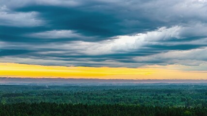Wall Mural - Hyperlapse of forest under dramatic sky with sunset hues in the background