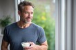 © Yevheniia - Caucasian mature male enjoying yogurt near window with nature view