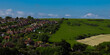 Village edge meets open countryside with traditional rooftops alongside farmland, concept of rural living, town boundary and transition between residential and agricultural land in England