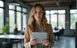 © nana - Curious woman holding tablet in modern office. High quality