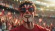 © Arda ALTAY - A joyful male sports fan with red and white face paint and sunglasses cheering in a crowded stadium.