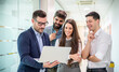 © Bojan - Group of business people standing in office hall holding laptop discussing project and developing company strategy