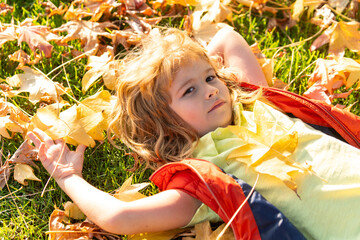 Wall Mural - Child portrait with autumn leaves. Little boy on a dreamy fall day in the autumn park. Childhood fun with falling maple leaves outdoors. Autumn day with a child. Kids face in autumn fall leaves.