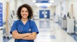 © Sabbir - Smiling nurse in blue scrubs with stethoscope stands confidently in a bright hospital corridor