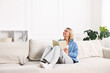 © New Africa - Woman reading book on sofa at home