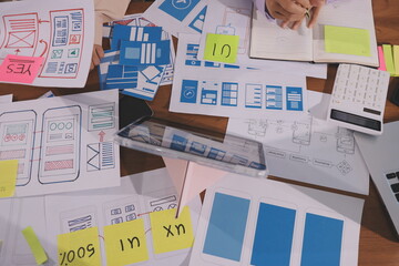 Close up ux developer and ui designer brainstorming about mobile app interface wireframe design on table with customer breif and color code at modern office.Creative digital development agency.