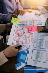 Close up ux developer and ui designer brainstorming about mobile app interface wireframe design on table with customer breif and color code at modern office.Creative digital development agency.