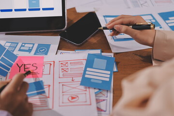 Close up ux developer and ui designer brainstorming about mobile app interface wireframe design on table with customer breif and color code at modern office.Creative digital development agency.