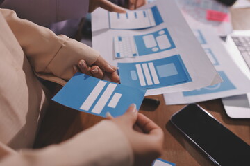 Close up ux developer and ui designer brainstorming about mobile app interface wireframe design on table with customer breif and color code at modern office.Creative digital development agency.