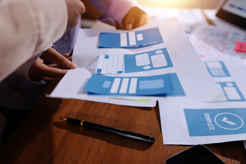 Close up ux developer and ui designer brainstorming about mobile app interface wireframe design on table with customer breif and color code at modern office.Creative digital development agency.