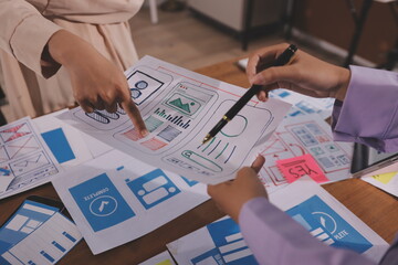 Close up ux developer and ui designer brainstorming about mobile app interface wireframe design on table with customer breif and color code at modern office.Creative digital development agency.