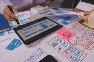 Close up ux developer and ui designer brainstorming about mobile app interface wireframe design on table with customer breif and color code at modern office.Creative digital development agency.