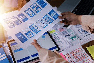 Close up ux developer and ui designer brainstorming about mobile app interface wireframe design on table with customer breif and color code at modern office.Creative digital development agency.