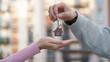 © Pavel - Close up of male property owner handing over house key with home shaped keychain to female client in front of apartment building. Concept of real estate deal, property purchase or apartment rental.