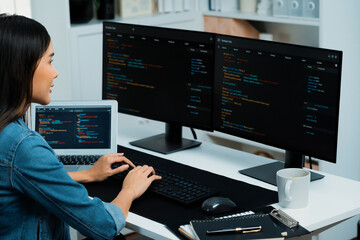 Young Asian in IT developer creating with typing online information on pc with coding program data of website application, wearing jeans shirt. surrounded by safety analysis two screens. Stratagem.